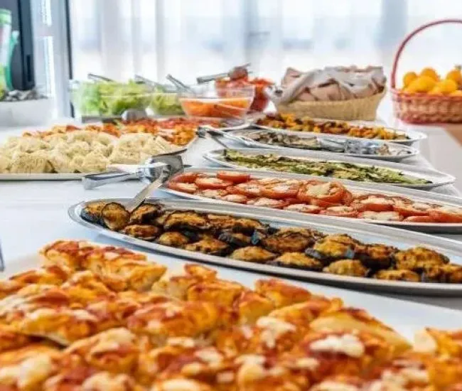 Buffet con piatti vari, verdure, frutta e pane su un tavolo bianco.