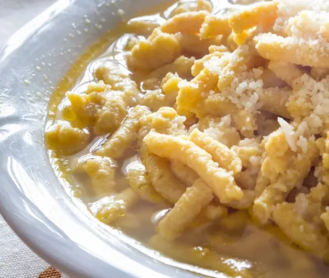Passatelli in brodo, un piatto tradizionale italiano con parmigiano grattugiato.