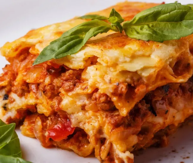 Lasagna al forno con carne, pomodoro e besciamella, guarnita con foglie di basilico fresco.